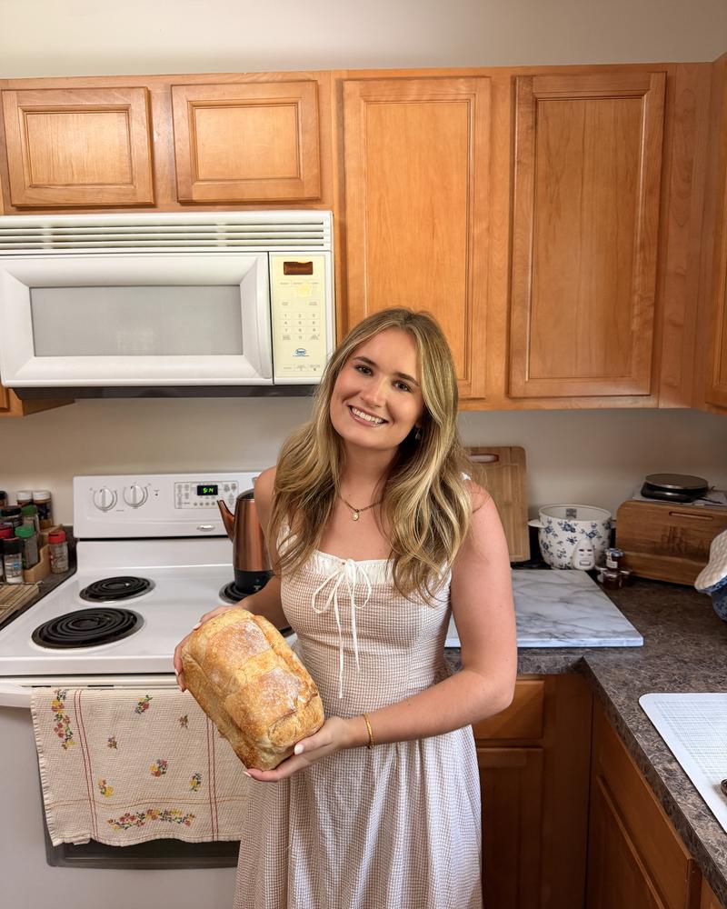 Gracyn holding a fresh-baked sourdough loaf in her kitchen